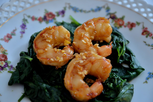 A plate with a flower design has 3 honey garlic shrimp on a bed of spinach.