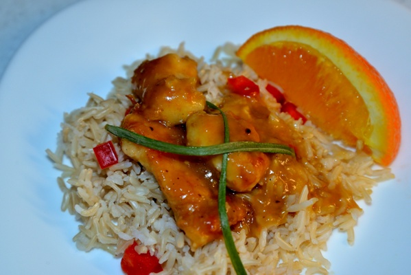 A dish containing orange chicken served on a bed of brown Basmati rice