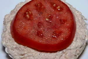 an open face bagel with cream cheese, tuna and tomato