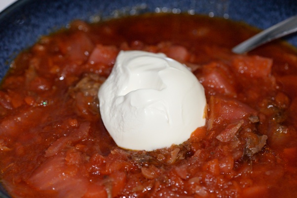 Beet and beef borscht in a blue bowl with a glob of sour cream